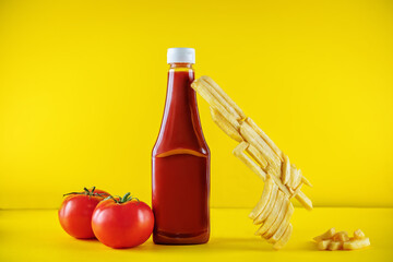 Tomato ketchup with French fries in the form of gun and fresh tomatoes on a yellow background