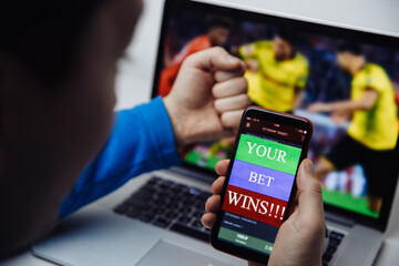 Male fan watching football play online broadcast on his laptop and celebrate victory in betting at bookmaker's website. Close-up.
