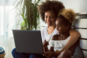 African American family. Mother and daughter using laptop computer at home or learning