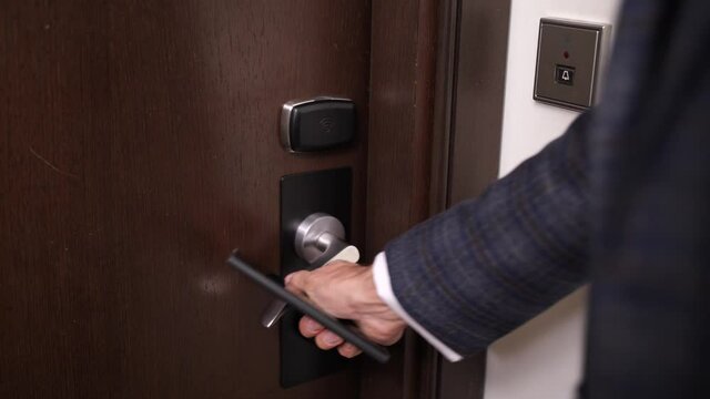 Close-up Of Male Hand Using Smartphone With Mobile App To Open Door Of Hotel Room. Midsection Of Businessman Opening Door With Electronic Lock By Attaching Cellphone And Entering Hotel Room