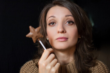 Obraz premium Female portrait of a girl holding chocolate star on stick and looking at the camera on black background in studio. Diet and food concept