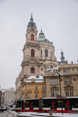 Fototapeta na wymiar Mostecka Street with a view of the Church of Saint Nicholas, old town with historical buildings, snow in winter day, Mala Strana or Lesser Town district, Prague, Czech Republic