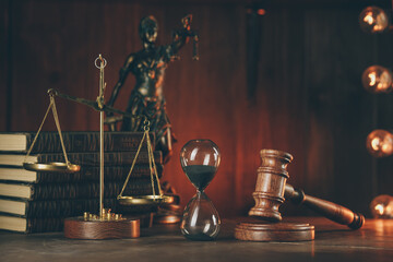 Wooden gavel, hourglass, books and lady of justice in dark room. Notary public tools.