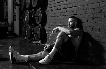 Young active strong sweaty fit muscular man with big muscles sitting on the gym floor and taking a...
