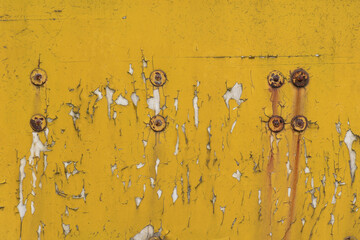 The metal surface, painted with yellow paint, is cracked with age and peeling in places. Rusty steel rivets with rust stains.