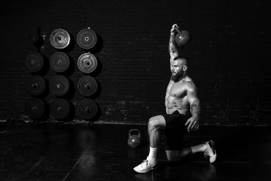 Young Active Sweaty Strong Muscular Fit Man With Big Muscles Doing One Leg Squat Workout With Heavy Kettlebell Above His Head In The Gym As Hardcore Cross Training Real People Exercise