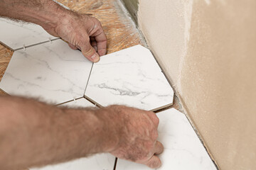 Renovation works - interior finishing worker (tiler) laying ceramic tiles on the floor