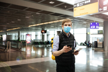 Digital vaccine passport. Hand holding mobile COVID-19 app for vaccination. Man wearing face mask. Covid pass for traveling. Phone in airport terminal in background. Vaccinated person ready for trip