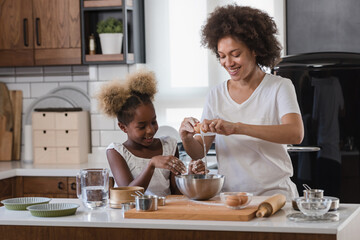 Fototapeta na wymiar Mother Teaching Child to Cook and Help in the Kitchen. African American Mother and Daughter making cookies at home. 