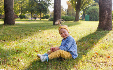 Naklejka na ściany i meble a little girl in a blue shirt sits and smiles on the grass in the park