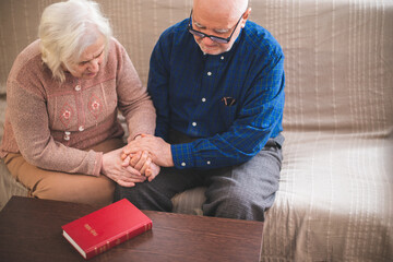 Elderly couple reading bible and pray together at home.
