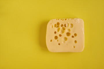 A small piece of cheese wrapped in a package lies on a yellow table 