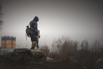 A post apocalypse soldier is walking on a abandoned area with a rifle and backpack. - obrazy, fototapety, plakaty