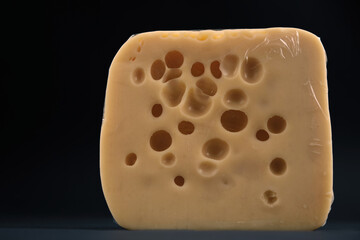 A small piece of cheese wrapped in a package is on a black background