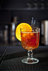 Orange cocktail on the bar. Mulled wine with white wine. Shelves with bottles of alcohol blurred in the background.