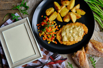 Chop with potatoes and vegetables on a wooden table and a frame for an inscription or photo