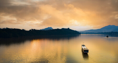 View from above, stunning aerial view of a tourist boat sailing along the Mekong river at sunset. Sunset Cruise is a slow-boat cruise along the Mekong river, Luang Prabang, Laos.
