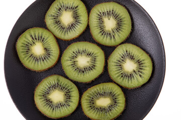 Ripe and green kiwi sliced with seeds visible on black plate