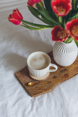 Breakfast in bed. A mug of coffee, a bouquet of tulips in a vase, a wooden tray. Women's Day. Spring.