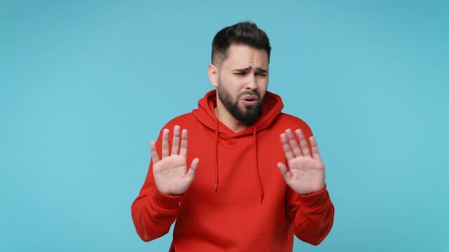 Confused bearded young man 20s years old in basic red streetwear hoodie isolated on blue background studio. People lifestyle concept. Pointing finger himself ask say who me no thanks i do not need it