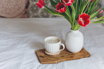 Breakfast in bed. A mug of coffee, a bouquet of tulips in a vase, a wooden tray. Women's Day. Spring.