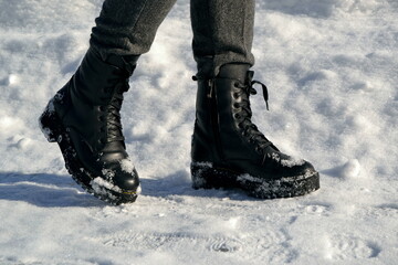 Woman's legs in high black boots walking down the street in snow