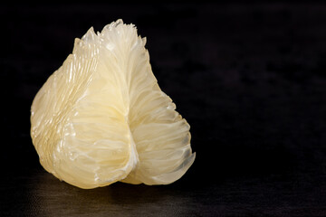 Piece of white pomelo fruit flesh on dark background. Fresh citrus fruit chunk.