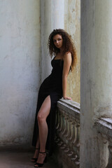 Beautiful young leggy curly brunette girl near white columns.