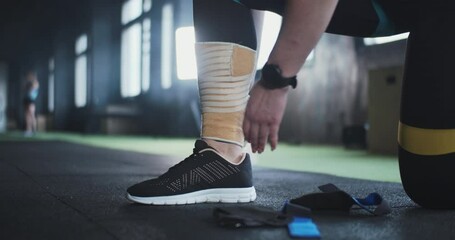 Sports medicine and technology. Close-up female athlete puts elastic knee wrap tape on leg, preparing for gym workout.