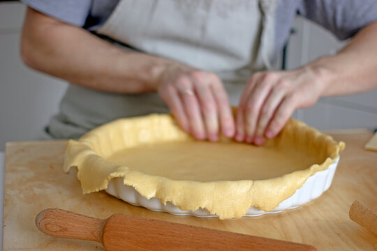 The process of making a base for a shortcrust quiche pie, male hands transfer a rolled dough sheet into a baking dish. Authentic home hobby home baker. Pie crust recipe