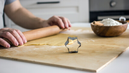 The process of making homemade asterisk shortbread cookies. Male hands cut cookies using a mold made of rolled dough. Authentic home hobby
