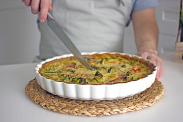 A French quiche pie in a baking dish on the kitchen table is cut into pieces with a knife. Homemade authentic baking with your own hands