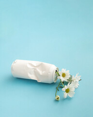 Minimalist composition on a blue background with a white can lying and flowers in it.