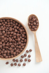 Chocolate corn balls in a wooden bowl and spoon scattered on a white background. Top view. Copy, empty space for text