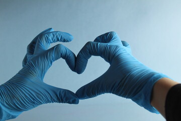 Hands doctor or nurse in blue medical gloves show a sign of heart love on a light blue background with a place to text a copyspace