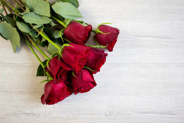 Beautiful bouquet of dark red roses on light wooden background, closeup with copyspace