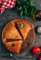 Italian food, closed pizza calzone with cheese, gray stone background.