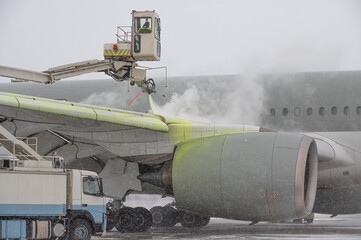 Winter at the airport. Snow storm. Airplane de-icing before take off. De-icing the aircraft before the flight. The de-icing machine sprinkles the wing of a passenger plane with de-icing fluid.