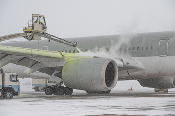 Winter at the airport. Snow storm. Airplane de-icing before take off. De-icing the aircraft before the flight. The de-icing machine sprinkles the wing of a passenger plane with de-icing fluid.