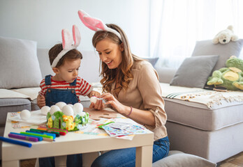 Happy family mother and child boy paints eggs for Easter at home. A photo of mother assisting boy...