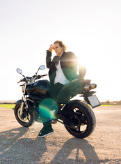 Fototapeta na wymiar Caucasian white man riding a black sporty biker style motorcycle with white t-shirt leather jacket with sunset light flashes