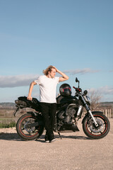 Caucasian white man leaning on a black sports bike with a white t-shirt daylight