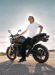 Fototapeta na wymiar Caucasian white man riding a black sports bike with white t-shirt and sun rays in sunset