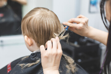 Hairdresser barbershop cuts the hair of blonde child boy with scissors. Haircut hairstyle close-up.