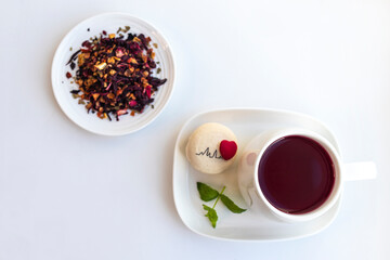 .Tea drink of hibiscus, dried apple, rose hips with the addition of orange peel, verbena, dried strawberries and pink pepper in a cup and macaroon on a white background, top view.