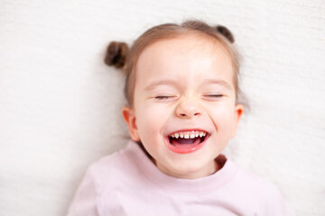 A girl European with blond hair happily and sincerely laughs with her eyes shut. Emotions are the joy of happiness. Large portrait in neutral tones