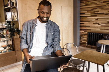 A happy African American man uses a laptop, looks at the screen, talks to someone via video chat, reads good news via email. Young business man is discussing a work plan. Work and business concept.