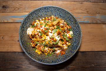 A delicious bowl of classic British chips or fries with gravy and garish on a wooden kitchen table background