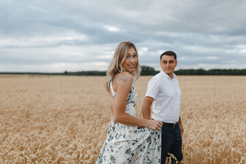 Smiling woman and man go across a wheat field holding hands. Lovers in the wheat field