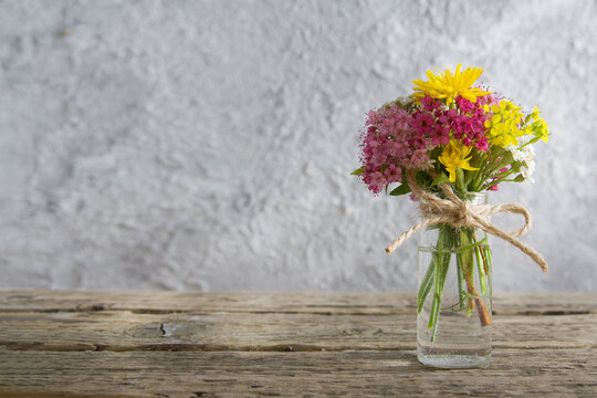 Miniature glass bottle with flowers on wooden table and concrete background with sunlight with copy space mother's day, 8 march greeting